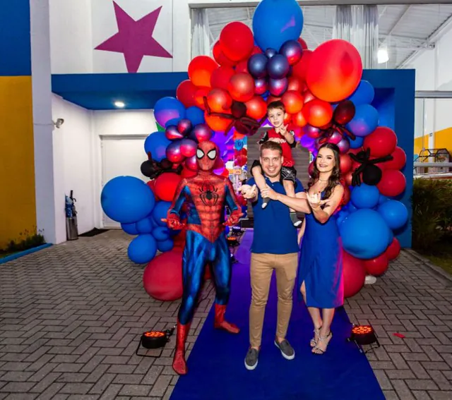Família e Homem-Aranha no tapete azul, sob um arco de balões vermelhos e azuis