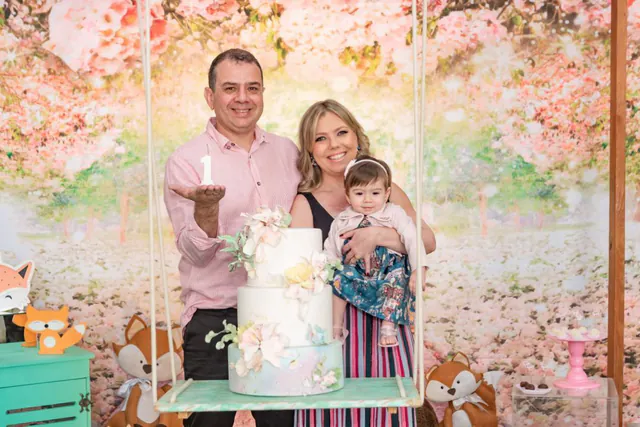 Tema jardim encantado: pais com a bebê ao lado do bolo de flores em um balanço decorado