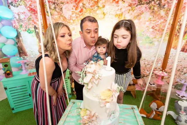 Tema jardim encantado: família soprando a vela de 1 ano do bolo com flores