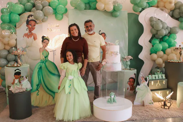 Tema Princesa Tiana: aniversariante de vestido verde com os avós ao lado do bolo