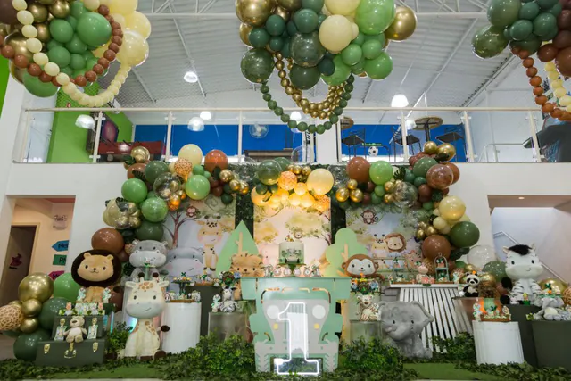 Salão decorado no tema safári, com arco de balões verdes e dourados e bichinhos de pelúcia
