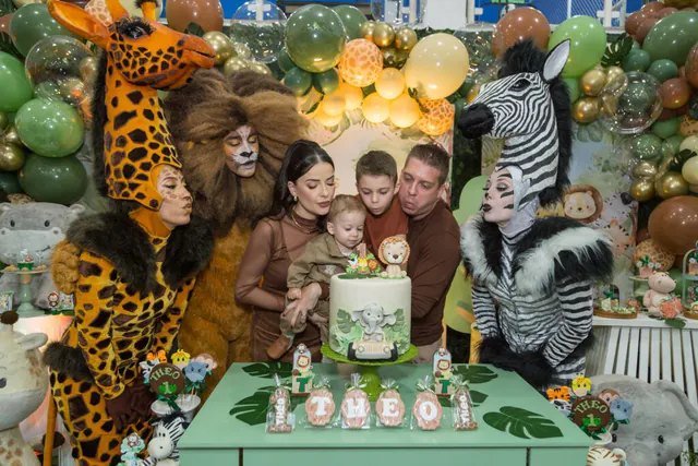 Tema safári: família soprando as velas do bolo de 1 ano com girafa, leão e zebra ao redor