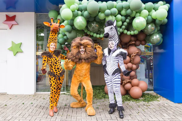 Girafa, leão e zebra fantasiados recebendo os convidados na entrada